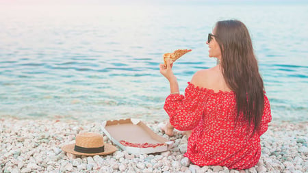 Woman eating pizza on the beach