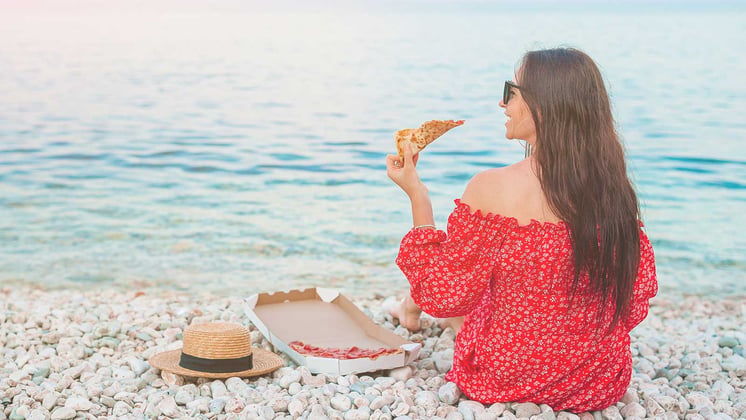 Woman eating pizza on the beach